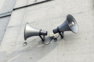 Pair of big retro loudspeakers mounted on grey concrete cement wall. Air raid nuclear strike alert speaker siren. Urgent or emergency announcement, message event. Dictatorship regime concept